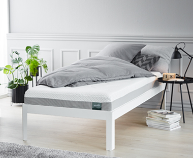 Pěnová matrace na posteli a šedé povlečení