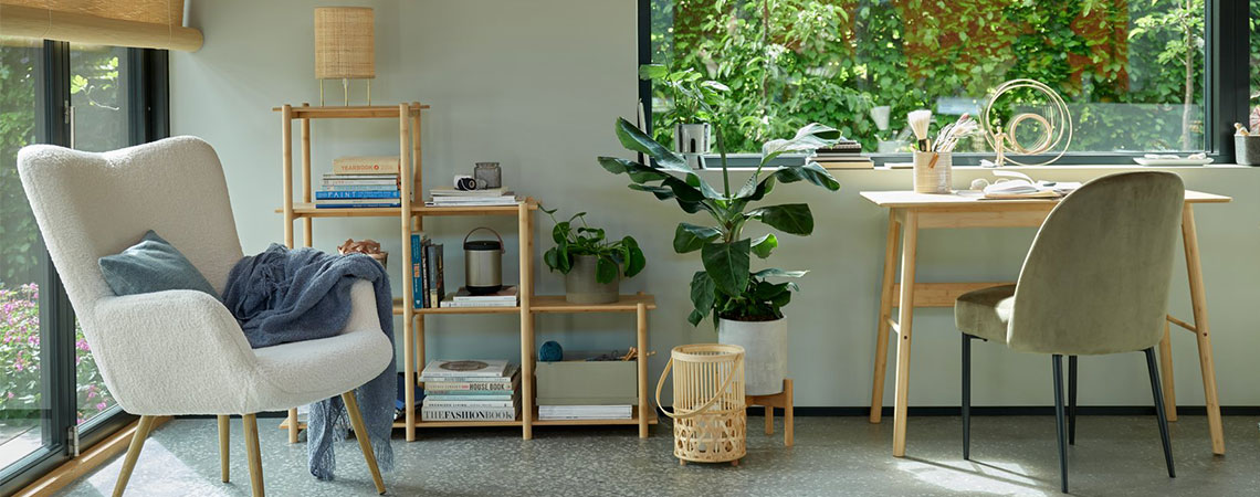 Béžové křeslo u okna a bambusová dělicí stěna v pozadí. Bambusová lucerna na zemi u psacího stolu a olivové zelené jídelní židle.