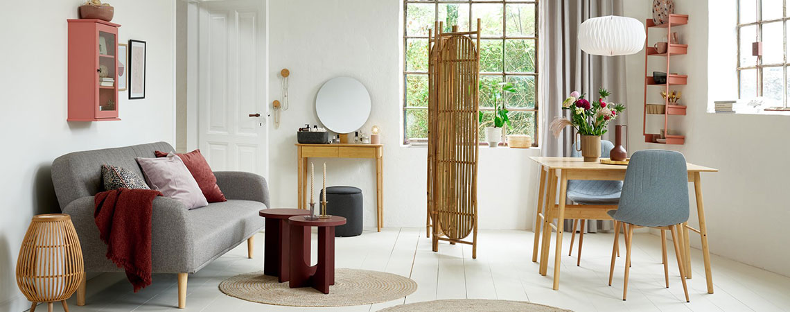 Jídelna a obývací pokoj s růžovou skříňkou, šedou rozkládací pohovkou, bambusovým toaletním stolkem a šedými jídelnými židlemi