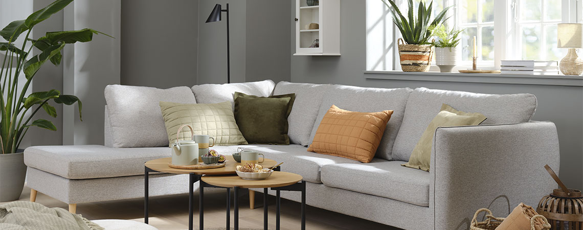 Obývací pokoj se šedou pohovkou, oranžovými, zelenými a šedými polštářky