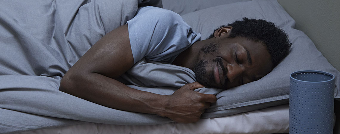 Muž spící v posteli s šedým polštářem a peřinou