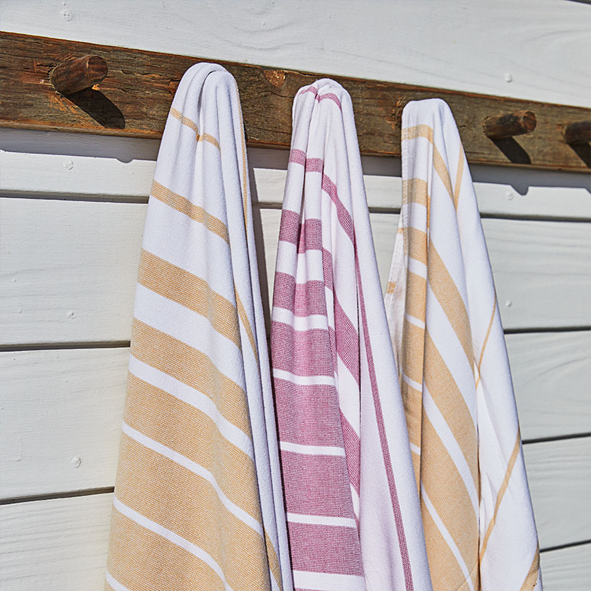Striped beach towels in white, orange, and pink fuchsia hanging on wooden wall