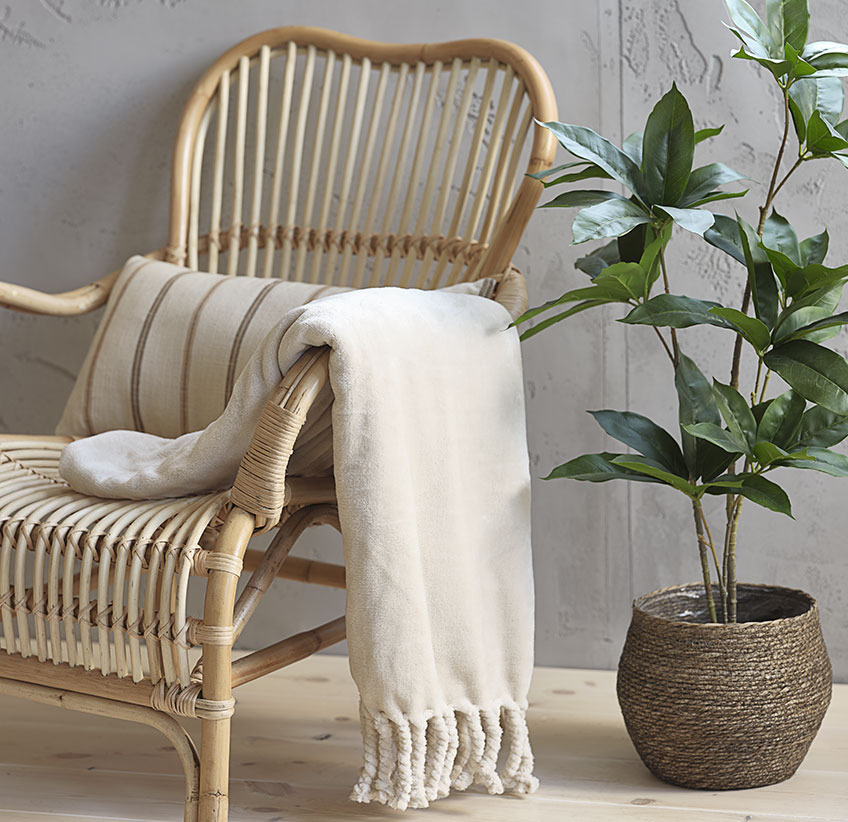 Beige throw on rattan lounge chair and artificial plant in plant pot 