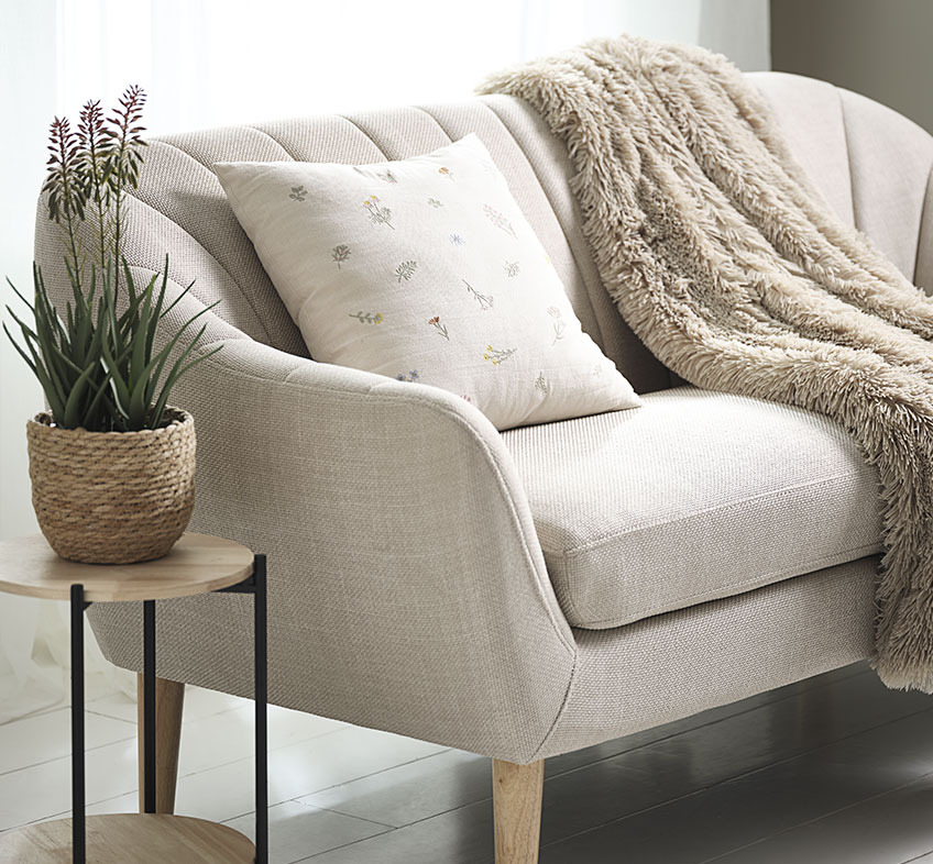 Artificial aloe vera plant with flowers, embroidered cushion, and faux fur throw on beige sofa 