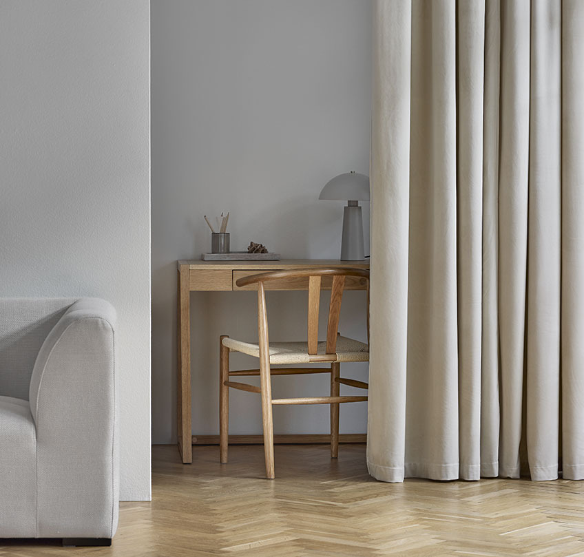 Grey curtains separating a home office with desk and office chair from a living room with an armchair and footstool