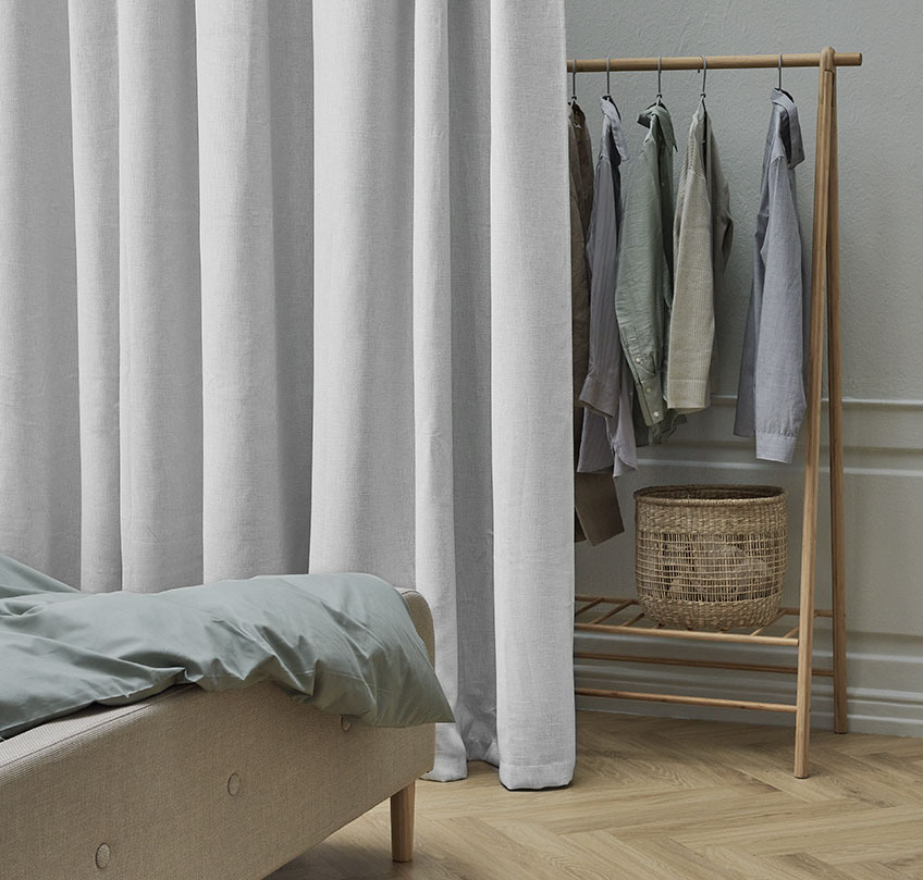 Beige curtain in front of a clothes rail separates a sleeping area from a wardrobe area