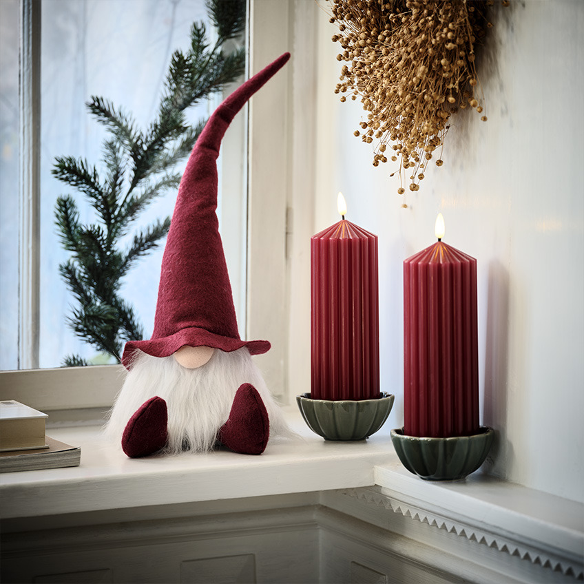 Scandinavian Christmas elf on windowsill next to large, red candles  