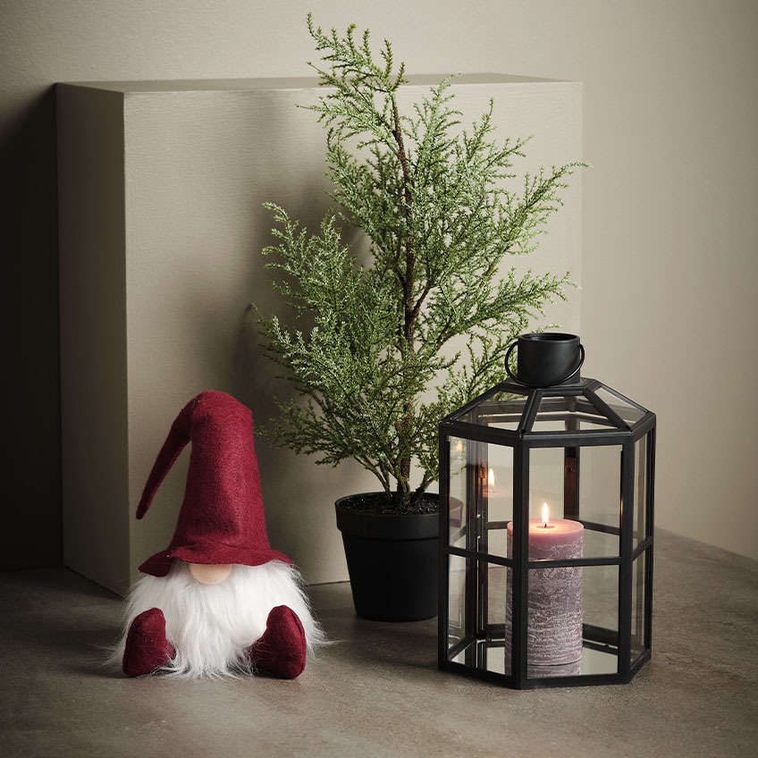 Scandinavian Christmas gnome next to artificial plant and lantern 