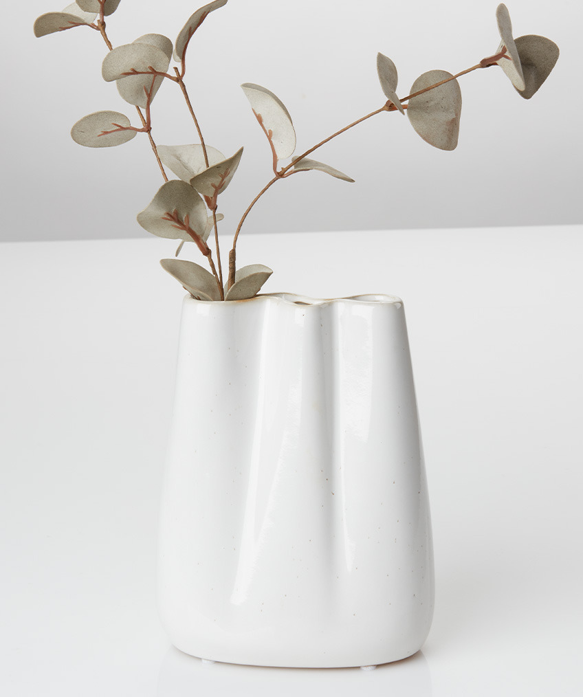 Bílá váza s organickými liniemi a zvlněnými okraji a umělou větvičkou
