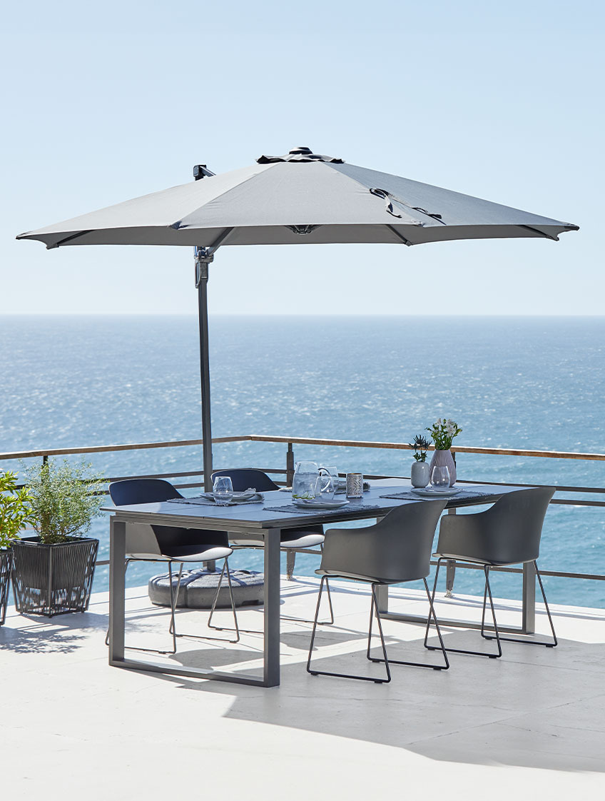 Velký závěsný slunečník a zahradní stůl a židle na terase u oceánu