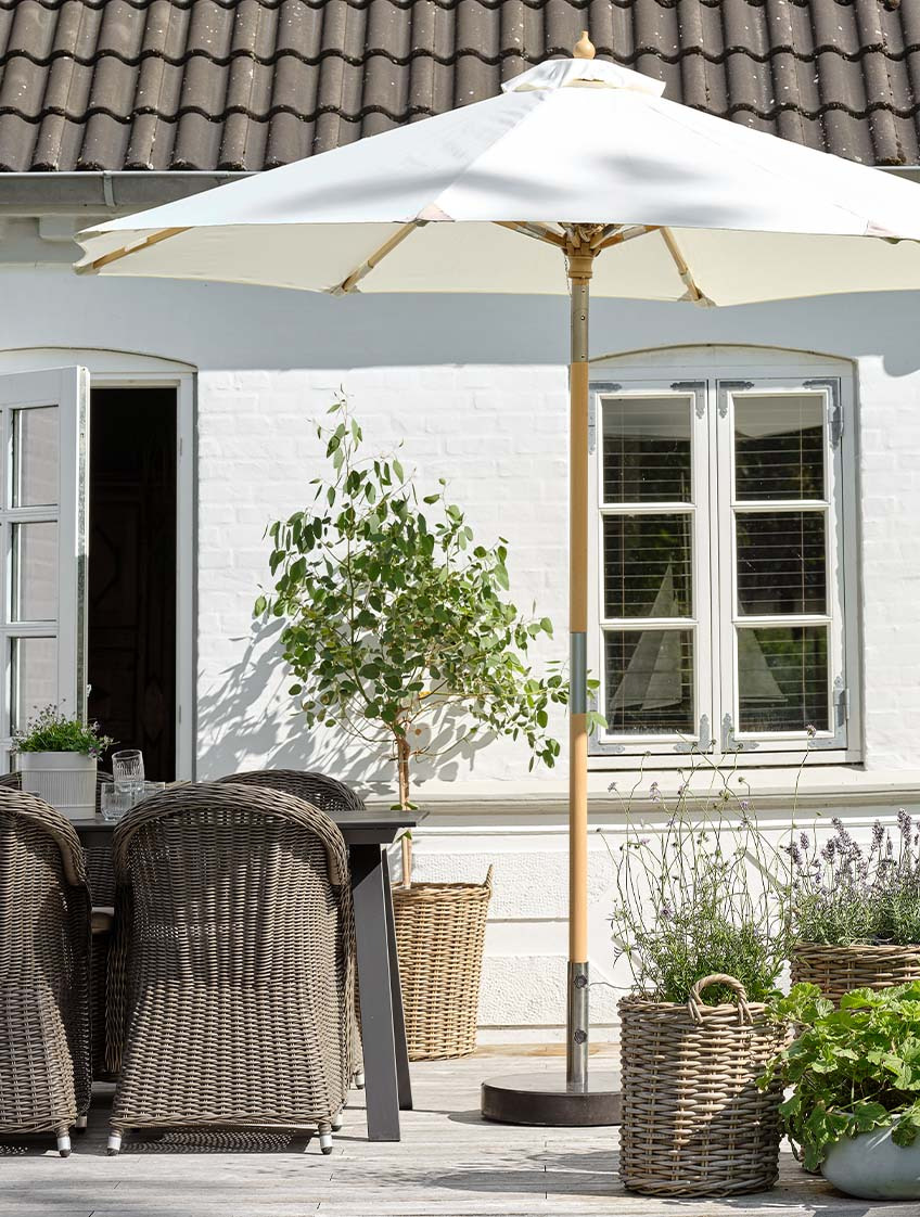 Klasický bílý zahradní slunečník na terase se zahradním stolem a zahradními židlemi