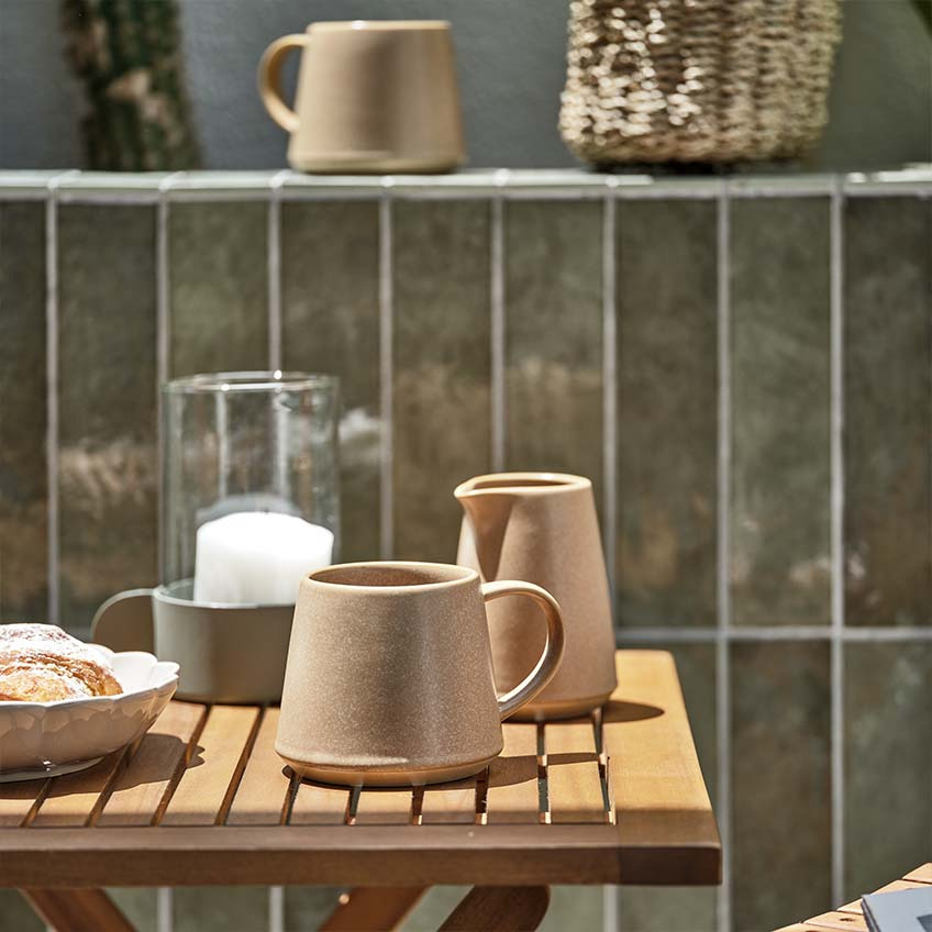 Hrnek na kávu a sklenice na mléko na malém dřevěném zahradním stole na plném slunci 