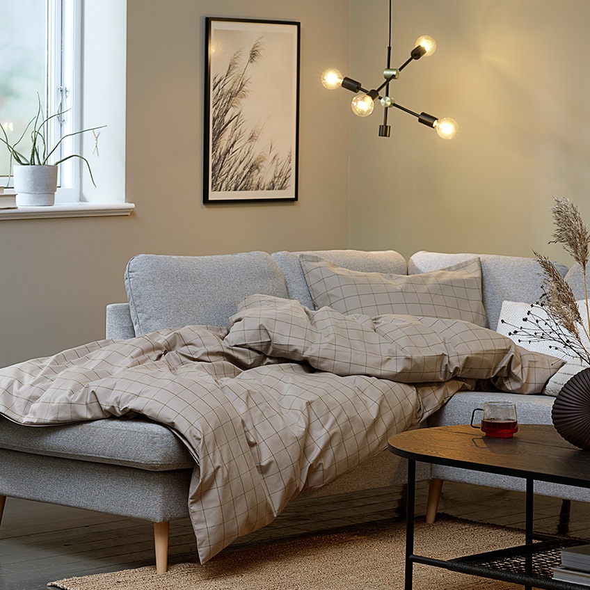 “hygge” v obývacím pokoji s velkou rohovou pohovkou, přikrývkou a osvětlením