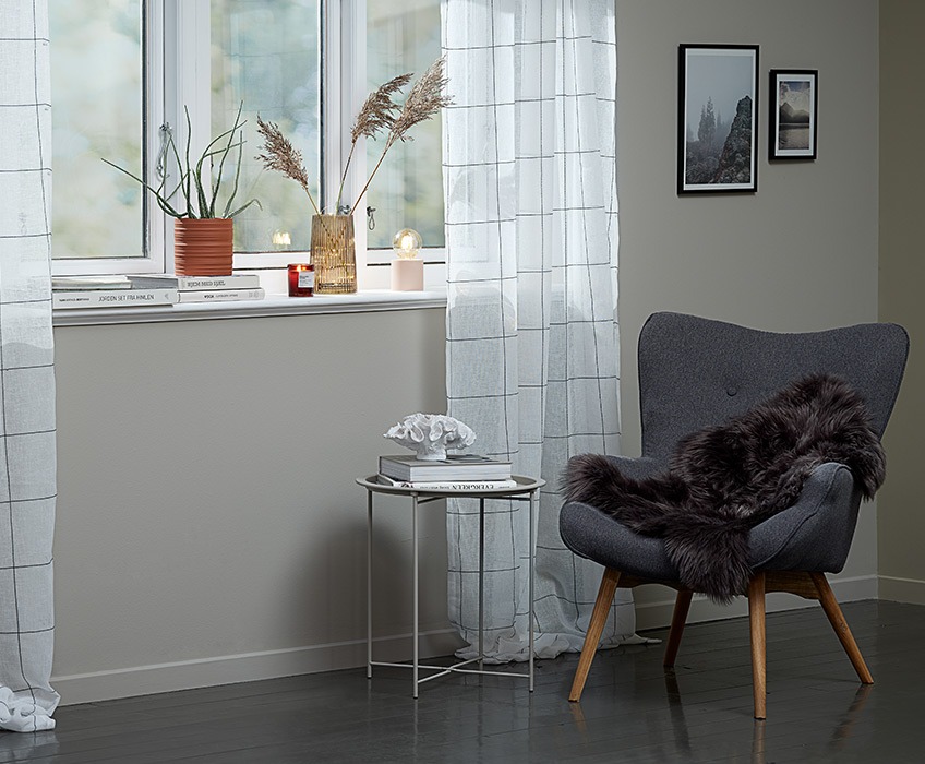 Lightweight curtains in front of a window with plant pot, scented candle, vase and battery lamp in the windowsill