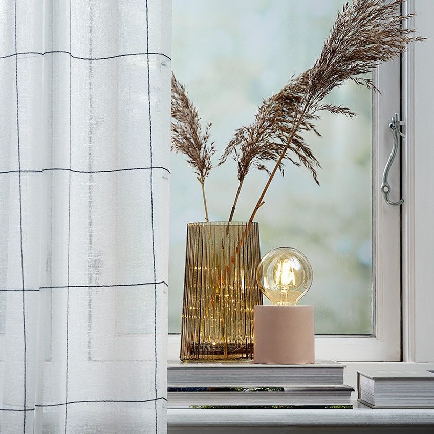 Lightweight curtains in a window with a vase and a battery lamp in the windowsill