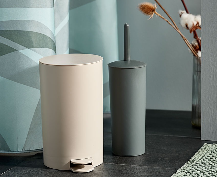 Toilet bin and toilet brush in front of a shower curtain in green colours