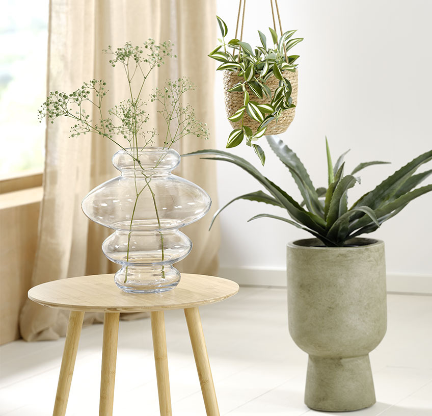 SYLVESTER vase, hanging STEFAN plant pot with ASGAR artificial plant and green SOLVI plant pot with CELIUS artificial plant Glass vase on an end table, hanging plant pot and green plant pot with artificial plants