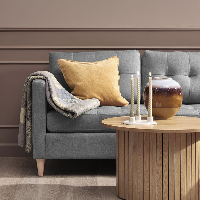 Quilted blanket and yellow cushion on grey sofa, wooden coffee table with candles and vase